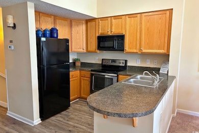 Kitchen featuring black appliances, dark countertops, a peninsula, dark wood-style flooring, and brown cabinets