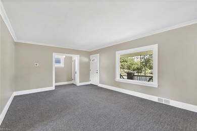 Another view of the living room featuring crown molding.  Original wood floors under carpet.  Large picture window floods the space with natural light.