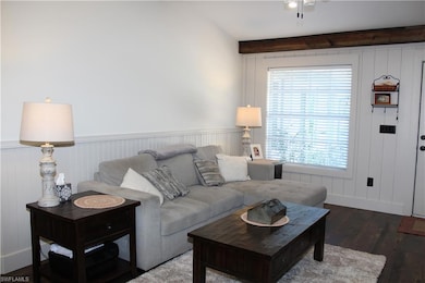Living room with dark wood-type flooring, beamed ceiling, and wainscoting