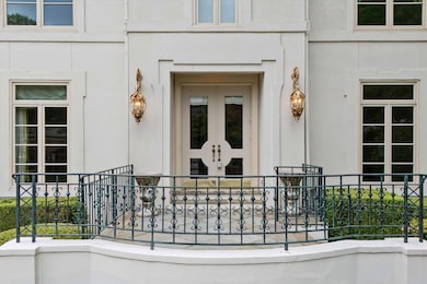 This Sophisticated Front Porch Welcomes Guests with Ornate Wrought Iron Railing, and Grand Double Doors Framed by Striking Lantern-Style Sconces. A Beautiful First Impression That Reflects the Timeless Charm and Quality of the Home.