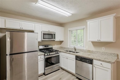 Kitchen with appliances with stainless steel finishes, a sink, light wood-type flooring, white cabinets, and a textured ceiling