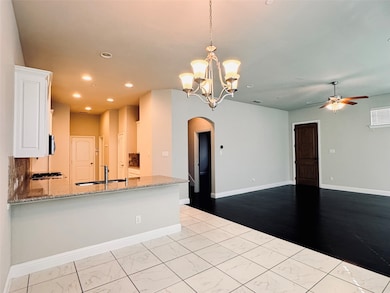 Kitchen with light stone countertops, arched walkways, white cabinets, ceiling fan, and hanging light fixtures