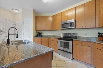 Kitchen with stainless steel appliances, light tile patterned floors, brown cabinetry, and dark stone countertops