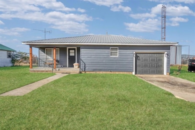 Single story home featuring concrete driveway, a front lawn, covered porch, a metal roof, and a garage