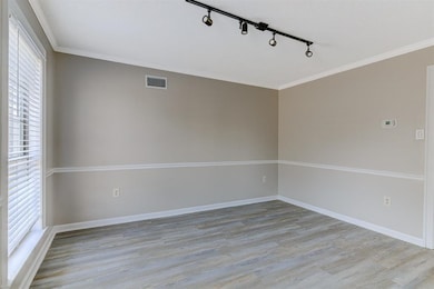 Empty room with ornamental molding, light wood finished floors, and track lighting