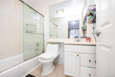 Bathroom with bath / shower combo with glass door, light tile patterned floors, and vanity