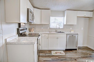Kitchen with appliances with stainless steel finishes, a sink, white cabinets, light countertops, and a textured ceiling