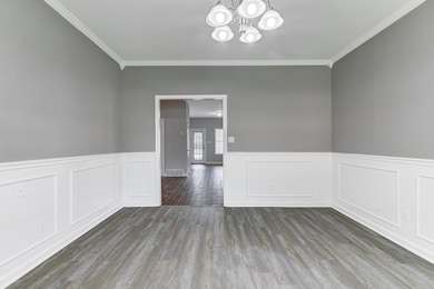 Unfurnished room with a decorative wall, a wainscoted wall, wood finished floors, a chandelier, and crown molding