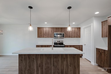 Kitchen with pendant lighting, a kitchen island with sink, stainless steel appliances, light wood-type flooring, and brown cabinets