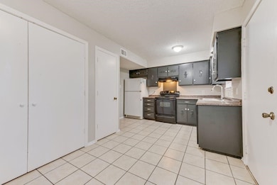 Kitchen featuring black electric range oven, a textured ceiling, light countertops, freestanding refrigerator, and light tile patterned floors