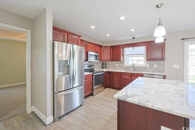 Kitchen with reddish brown cabinets, light stone countertops, appliances with stainless steel finishes, tasteful backsplash, and pendant lighting