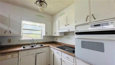 Kitchen featuring white appliances, a sink, under cabinet range hood, white cabinetry, and a textured ceiling
