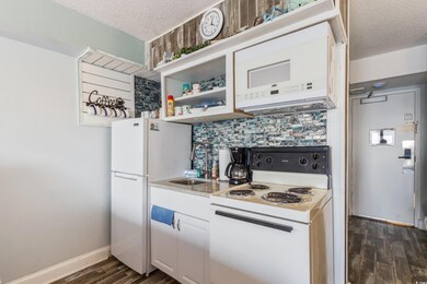 Kitchen featuring a textured ceiling, white appliances, backsplash, light countertops, and dark wood-type flooring