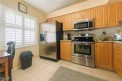 Kitchen featuring appliances with stainless steel finishes, light stone counters, light tile patterned floors, and decorative backsplash