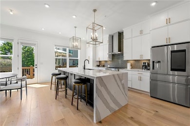 Kitchen featuring stainless steel refrigerator with ice dispenser, wall chimney range hood, a sink, a chandelier, and a center island with sink