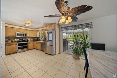 Kitchen featuring appliances with stainless steel finishes, light tile patterned floors, backsplash, a ceiling fan, and light brown cabinets