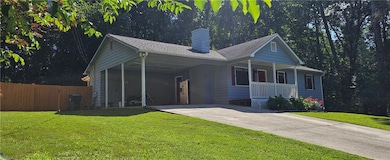 View of front of property with concrete driveway, covered porch, a carport, and a chimney