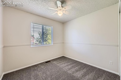 Carpeted empty room with a textured ceiling, a ceiling fan, and baseboards