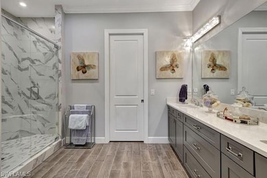 Primary bath with frameless glass enclosed shower, porcelain tiled flooring, vanity with dual sinks, and quartz countertopsvanity, porcelain tile plank wood like floor,  crown molding and walk-in-closet