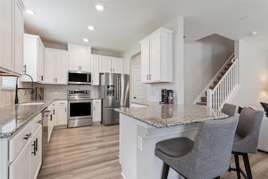 Kitchen featuring appliances with stainless steel finishes, a kitchen breakfast bar, white cabinetry, light stone countertops, and recessed lighting