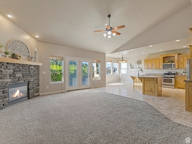 Unfurnished living room featuring light colored carpet, a stone fireplace, light tile patterned floors, ceiling fan, and recessed lighting