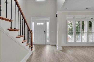 Foyer entrance with light wood-style flooring, crown molding, healthy amount of natural light, stairs, and wainscoting