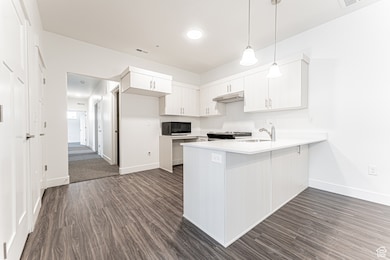 Kitchen with under cabinet range hood, a peninsula, range, baseboards, and dark wood-style flooring