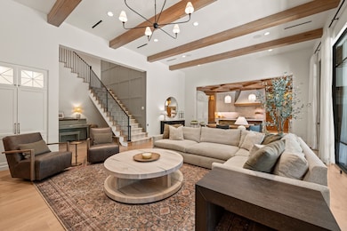 The main living area blends warmth with sophistication, anchored by a fireplace flanked with softly lit built-ins that add both storage and charm. Floor-to-ceiling windows and iron framed doors flood the space with natural light while offering a clear view of the backyard, creating a seamless connection between indoors and out. Exposed wood beams add architectural interest and tie the living area into the adjacent kitchen and dining spaces, making it all feel cohesive and intentional. Whether you're gathered around the fire or entertaining with ease, this space was designed to feel effortlessly livable.