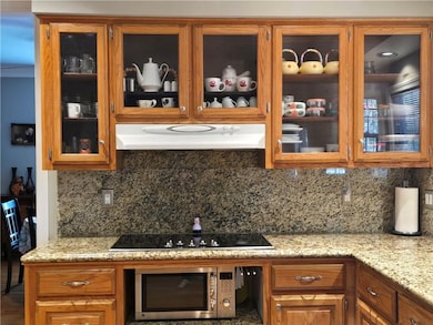 Kitchen featuring brown cabinetry, glass insert cabinets, decorative backsplash, and stainless steel microwave