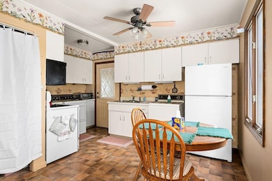 Kitchen with freestanding refrigerator, decorative backsplash, white cabinets, and ceiling fan