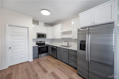 Kitchen featuring open shelves, white cabinets, gray cabinetry, stainless steel appliances, and a sink