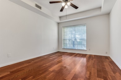 Empty room featuring dark wood finished floors, ceiling fan, and a tray ceiling