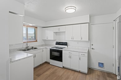 Kitchen featuring range with electric stovetop, white cabinets, light countertops, light wood-style flooring, and a textured ceiling