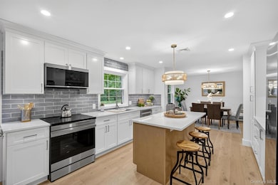 Kitchen with stainless steel appliances, light wood-style floors, tasteful backsplash, a kitchen island, and white cabinetry