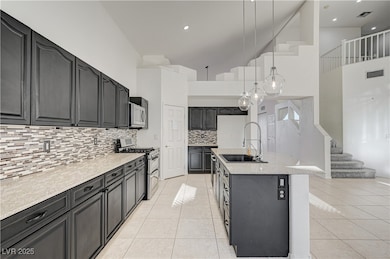 Kitchen featuring pendant lighting, stainless steel appliances, light tile patterned flooring, a center island with sink, and high vaulted ceiling