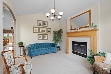 Living area with a chandelier, carpet, a fireplace with flush hearth, vaulted ceiling, and arched walkways