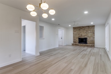 Unfurnished living room featuring light wood-type flooring, recessed lighting, a ceiling fan, a brick fireplace, and a chandelier