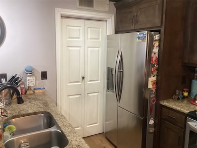 Kitchen with appliances with stainless steel finishes, dark brown cabinetry, light wood-type flooring, light stone countertops, and a textured wall