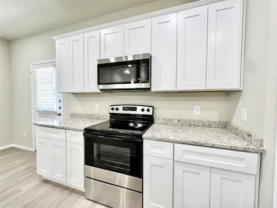 Kitchen featuring appliances with stainless steel finishes, white cabinetry, light stone counters, and light wood finished floors