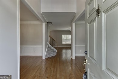 Entryway featuring dark wood-style floors, crown molding, stairway, wainscoting, and a decorative wall
