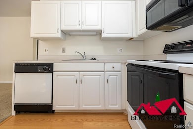Kitchen with range with electric stovetop, black microwave, white cabinets, dishwasher, and light countertops