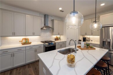 Kitchen featuring stainless steel appliances, a sink, wall chimney range hood, light stone countertops, and recessed lighting