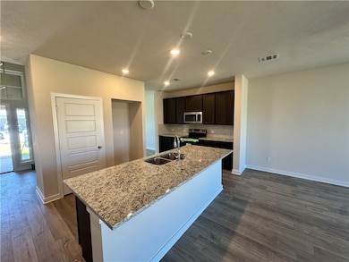 Kitchen featuring light stone counters, appliances with stainless steel finishes, dark brown cabinets, dark wood-type flooring, and a textured ceiling
