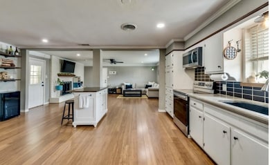 Kitchen with open floor plan, white cabinetry, stainless steel appliances, a kitchen breakfast bar, and ornamental molding
