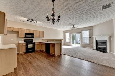 Kitchen with black appliances, a fireplace with flush hearth, open floor plan, light countertops, and a chandelier
