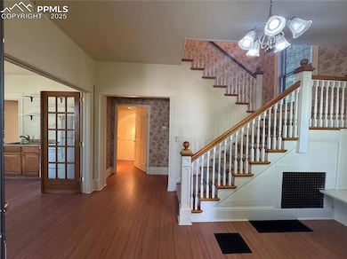 Stairway with wallpapered walls, wood finished floors, and a chandelier