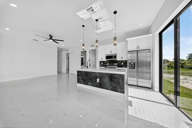 Kitchen with light marble finish floors, pendant lighting, appliances with stainless steel finishes, a kitchen island with sink, and white cabinets