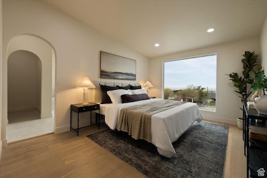 Bedroom with wood finished floors, arched walkways, baseboards, lofted ceiling, and recessed lighting