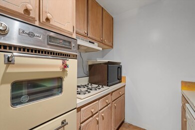 Kitchen with white appliances, light countertops, light tile patterned floors, under cabinet range hood, and brown cabinets