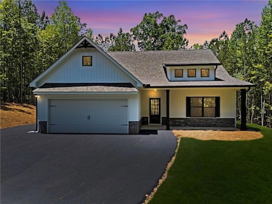 View of front of property featuring asphalt driveway, a shingled roof, an attached garage, stone siding, and a front yard